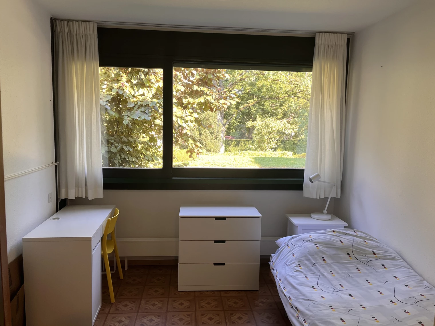 Une chambre avec un lit, une table de chevet, un bureau avec une chaise et une grande fenêtre