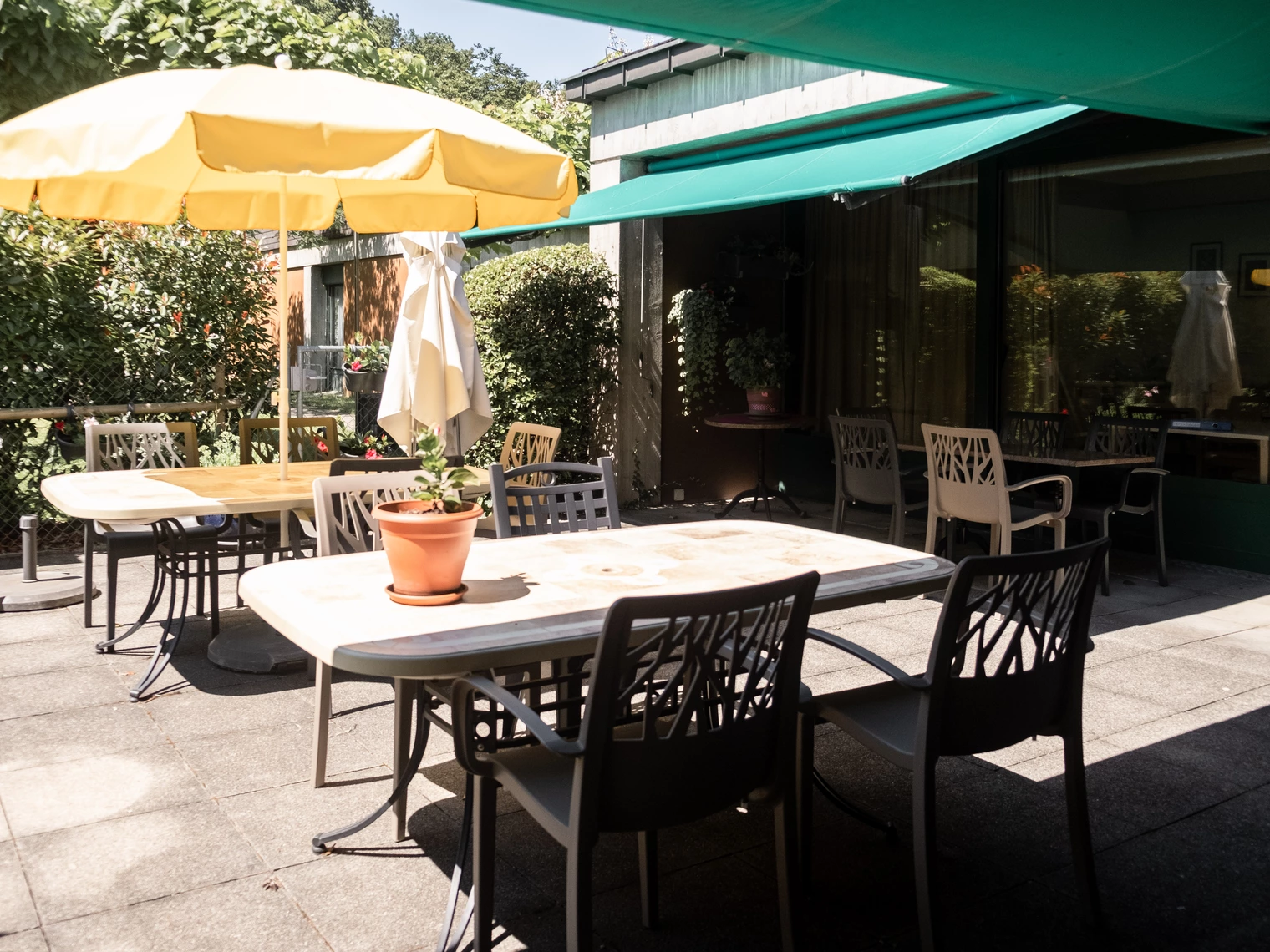 Une terrasse ensoleillée avec des tables, des chaises et un parasols 