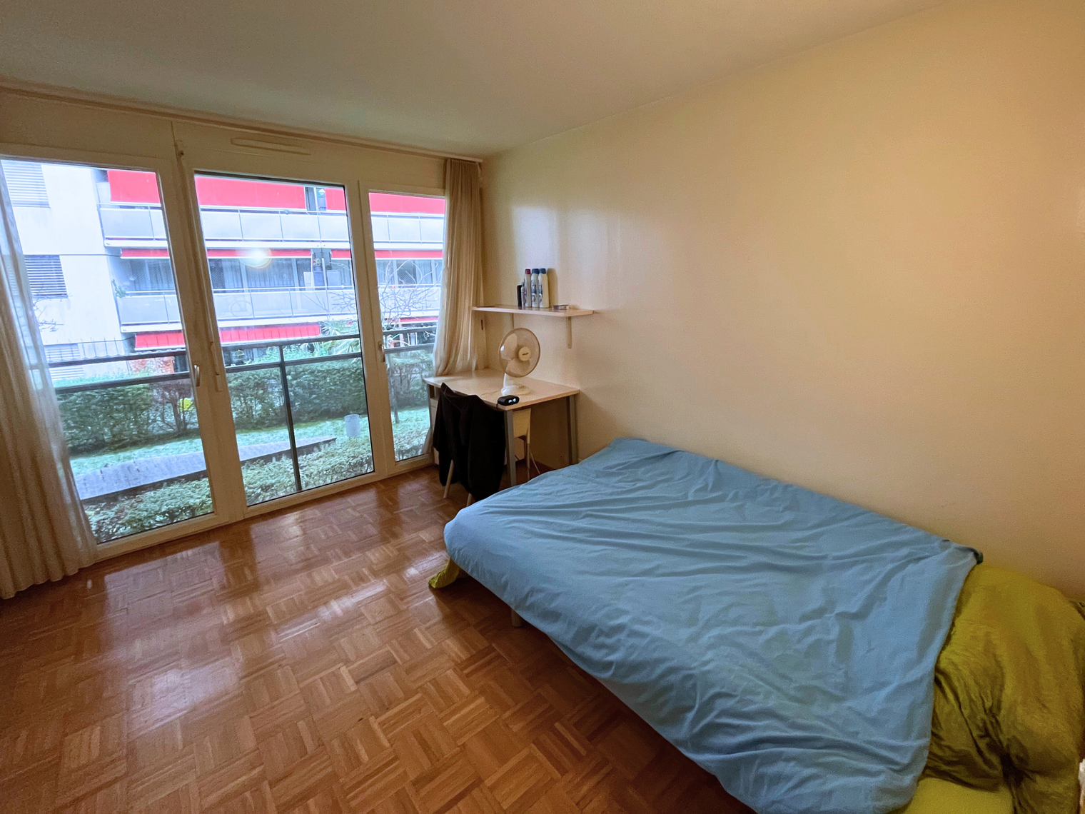 Une chambre avec une grande baie vitrée, un lit, un bureau avec une étagère et une chaise