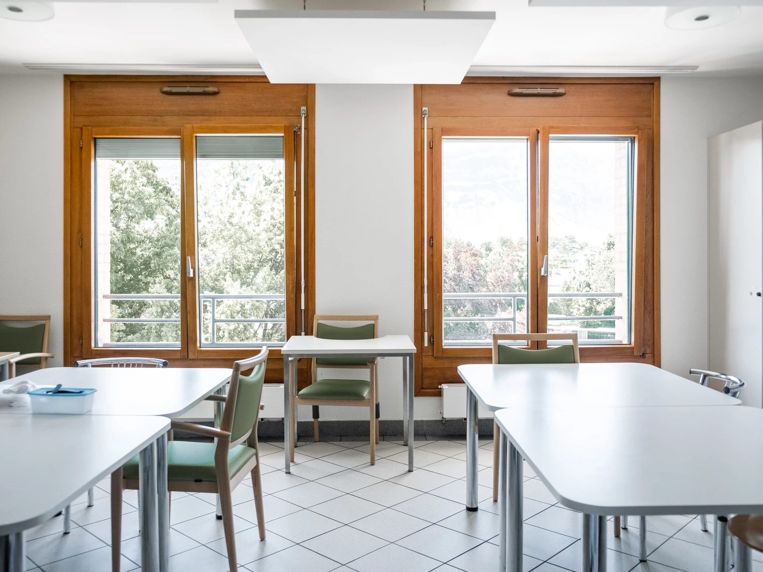 Une salle d'activités avec deux tables avec des chaises et deux grandes fenêtre