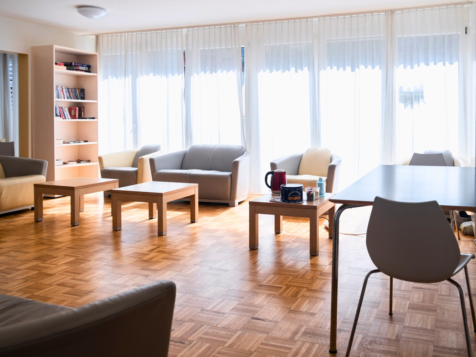 Un salon lumineux avec un bibliothèque, des canapés et fauteuils, des tables basse et une table et des chaises